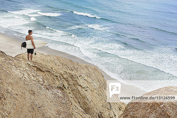 Man carrying surfboard while standing on rock formation at beach