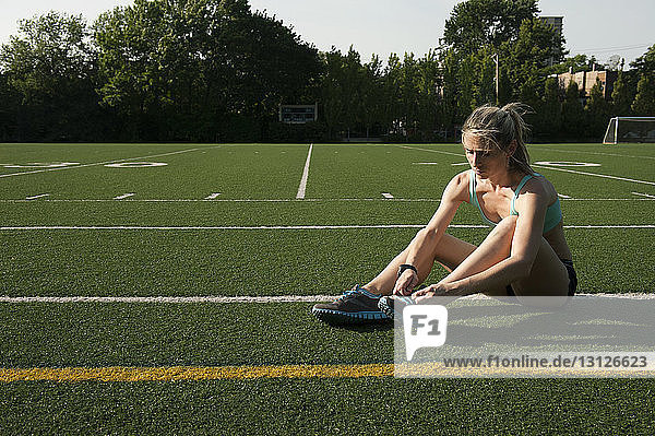 Weibliche Sportlerin beim Schnürsenkelbinden auf dem Sportplatz sitzend