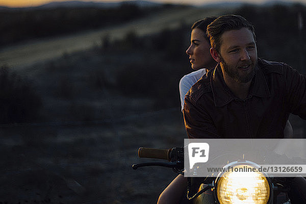Young couple riding illuminated motorcycle at field