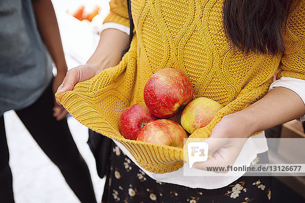Midsection of woman carrying apples in sweater at market