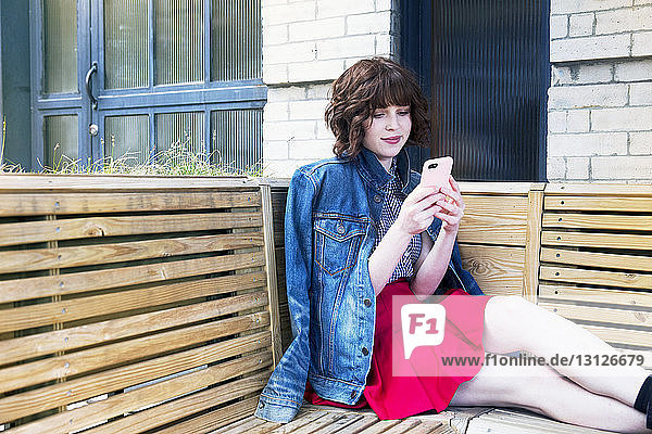 Frau benutzt Smartphone  während sie auf einer Bank an der Wand sitzt