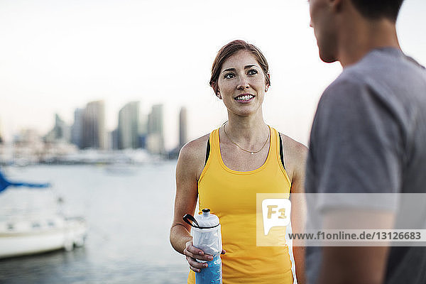 Sportliche Frau spricht mit Mann  während sie eine Wasserflasche am Hafen hält