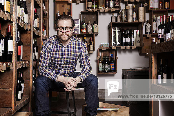 Porträt eines selbstbewussten männlichen Besitzers  der mit gefalteten Händen im Weinladen sitzt