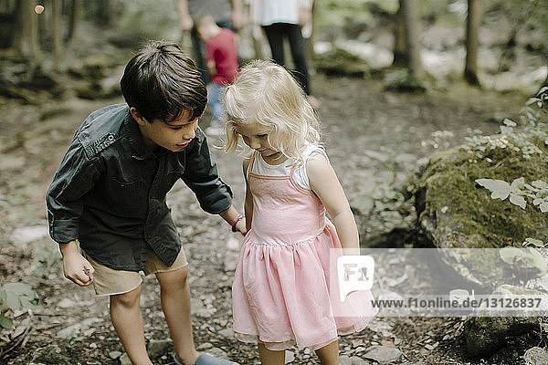 Siblings talking while family standing in background at forest