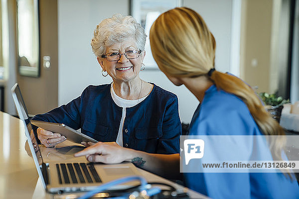 Glückliche ältere Frau  die eine häusliche Pflegekraft ansieht  während sie einen Tablet-Computer hält