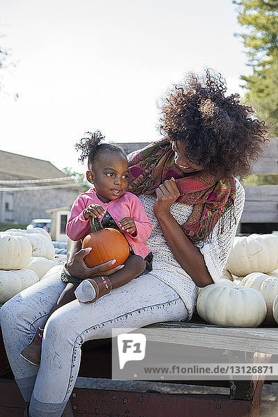 Glückliche Mutter sieht Tochter an  während sie Kürbis auf Biobauernhof hält