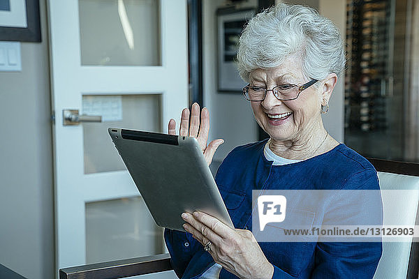 Happy senior woman video conferencing through tablet computer at home