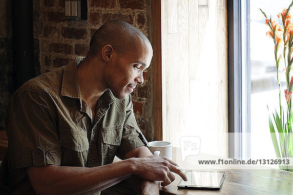 Mann benutzt Tablet-Computer  während er im Café am Tisch sitzt