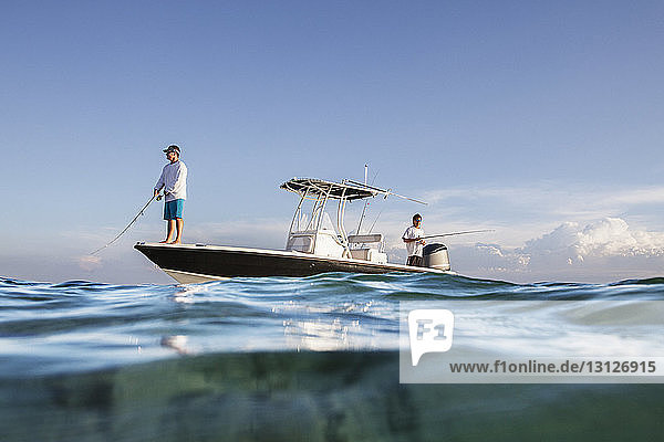 Tiefblick auf Männer  die fischen  während sie auf einem Boot auf See gegen den Himmel stehen