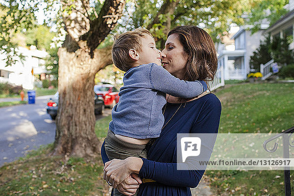 Mother kissing cute son while standing against trees