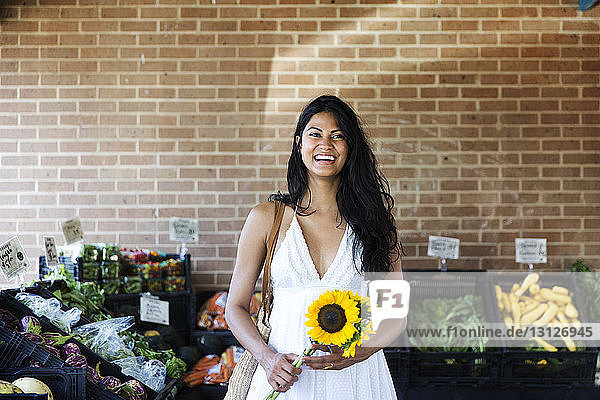 Happy woman holding sunflowers while standing at market