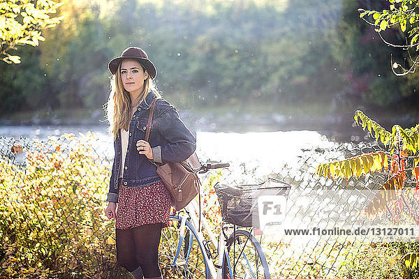Portrait of woman with bicycle standing in park
