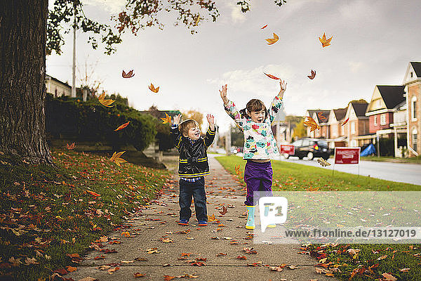 Fröhliche Geschwister mit erhobenen Armen auf dem Fußweg im Herbst
