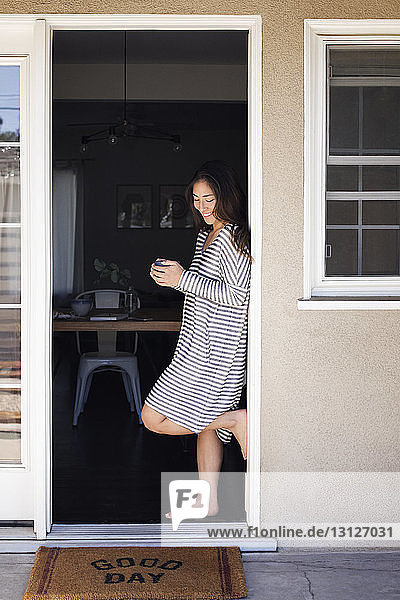 Glückliche Frau hält Kaffeetasse  während sie an der Tür steht