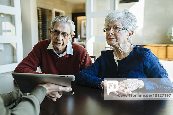 Ausgeschnittenes Bild eines Finanzberaters  der einem älteren Ehepaar den Plan auf einem Tablet-Computer im Büro erklärt