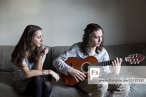 Frau schaut ihren auf dem Sofa sitzenden Bruder beim Gitarrespielen an