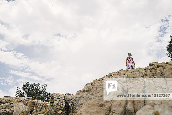 Tiefwinkelansicht eines Mädchens  das auf Felsen vor bewölktem Himmel steht