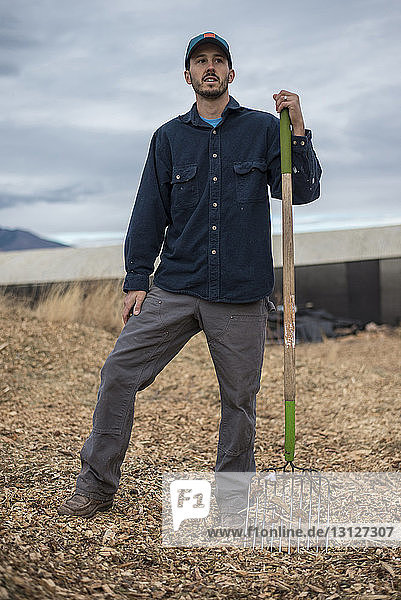 Full length of man holding gardening fork while standing on field against sky