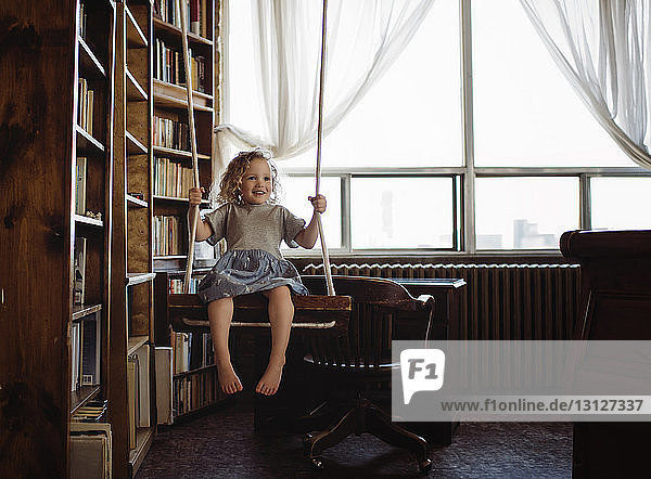 Glückliches Mädchen schaukelt zu Hause an Bücherregalen