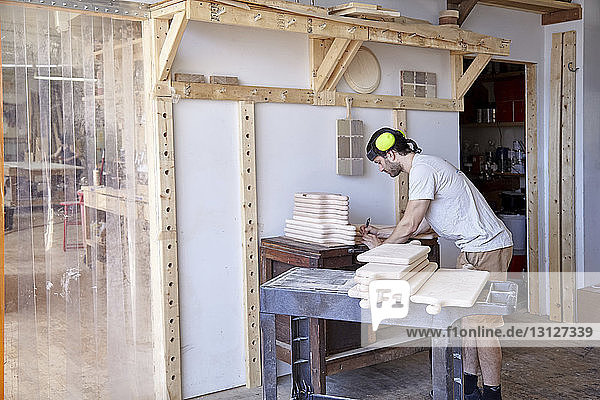 Seitenansicht eines Tischlers mit Gehörschutz bei der Arbeit in der Werkstatt an der Wand