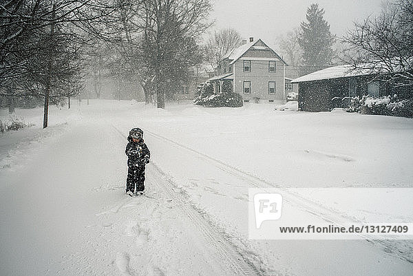 Boy standing on snow covered field during snowfall