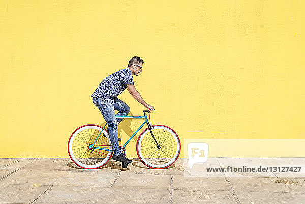 Seitenansicht eines Fahrrad fahrenden Mannes gegen gelbe Wand auf dem Bürgersteig in der Stadt