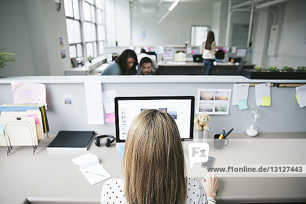 Rückansicht einer Geschäftsfrau am Desktop-Computer mit Kollegen im Hintergrund
