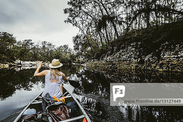 Rückansicht einer jungen Frau  die mit einem Ruderboot auf einem See im Wald rudert