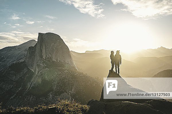 Paar  das an einem sonnigen Tag auf einer Klippe vor den Bergen steht