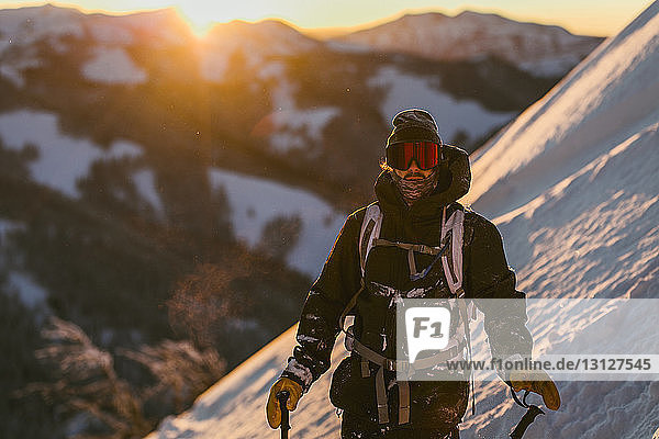 Mann in Skikleidung steht bei Sonnenuntergang auf schneebedecktem Berg