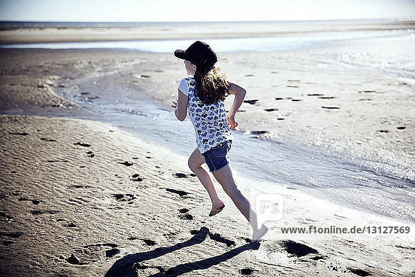 Verspieltes Mädchen rennt am Strand an einem sonnigen Tag