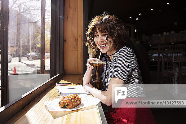 Porträt einer glücklichen Frau  die im Café Cola trinkt