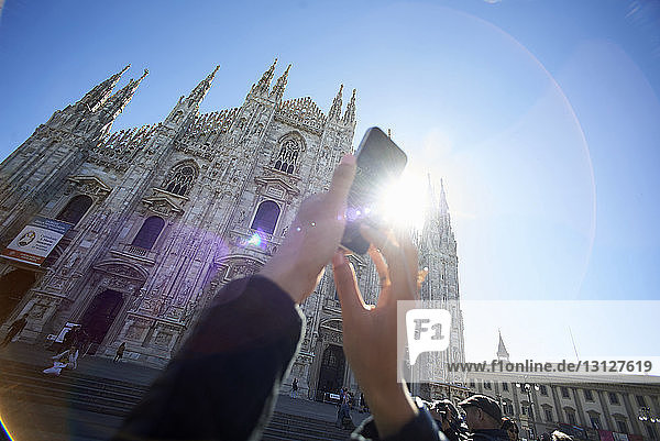 Cropped image of woman photographing Duomo Di Milano against clear blue sky
