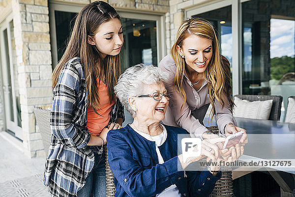Mittlere erwachsene Frau  die mit Mutter und Tochter auf der Veranda ein Smartphone benutzt