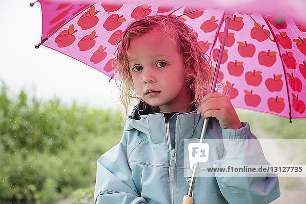 Porträt eines süßen Mädchens mit rosa Regenschirm  das in der Regenzeit vor Pflanzen steht