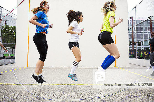 Side view of women performing double Dutch against wall