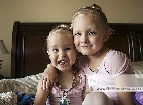 Portrait of happy sisters in ballet costumes sitting on bed at home