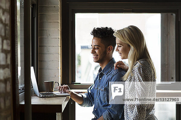 Lächelndes Paar mit Laptop  während es im Café am Fenster sitzt