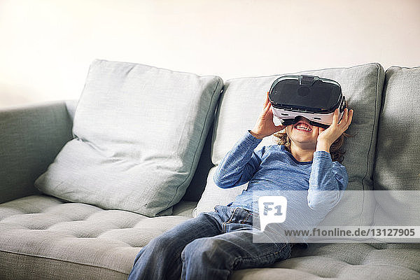 Glücklicher Junge mit Virtual-Reality-Simulator  der zu Hause auf dem Sofa sitzt