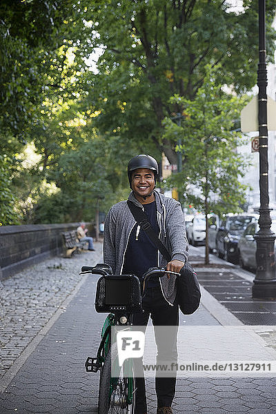 Portrait of happy man with bicycle standing on footpath in city