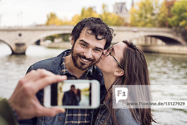 Ausschnitt eines Freundes  der ein Paar mit einem Smartphone am Fluss fotografiert