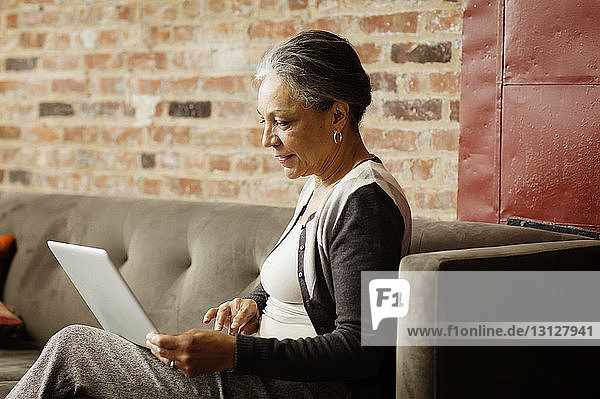 Seitenansicht einer Geschäftsfrau  die einen Laptop-Computer benutzt  während sie im Büro auf dem Sofa sitzt
