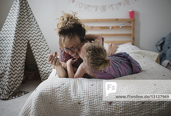 Tochter küsst glückliche Mutter  während sie zu Hause im Bett liegt