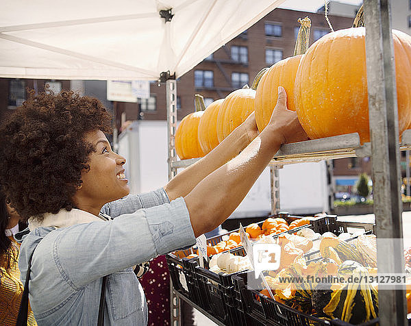 Woman picking up pumpkin from shelf in market