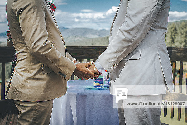 Mittelteil eines homosexuellen Paares  das sich an der Hand hält  während es am Tisch steht