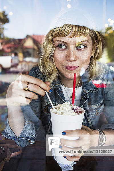 Nachdenkliche Frau schaut weg  während sie im Café ein Milchshake-Glas hält