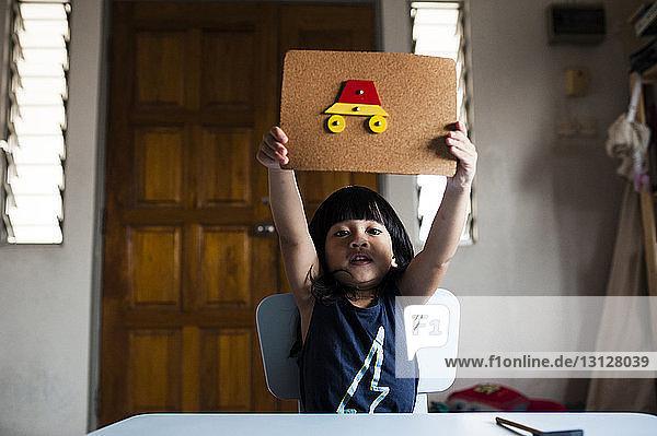 Porträt eines süßen Jungen  der am Tisch sitzend Kunsthandwerk aus Karton zeigt