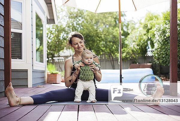Happy mother holding baby while sitting with legs apart on mat