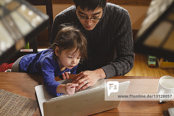 High angle view of father with cute daughter using laptop computer on wooden table at home