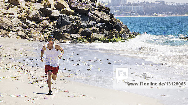 Mann mit Sonnenbrille joggt am Strand an einem sonnigen Tag